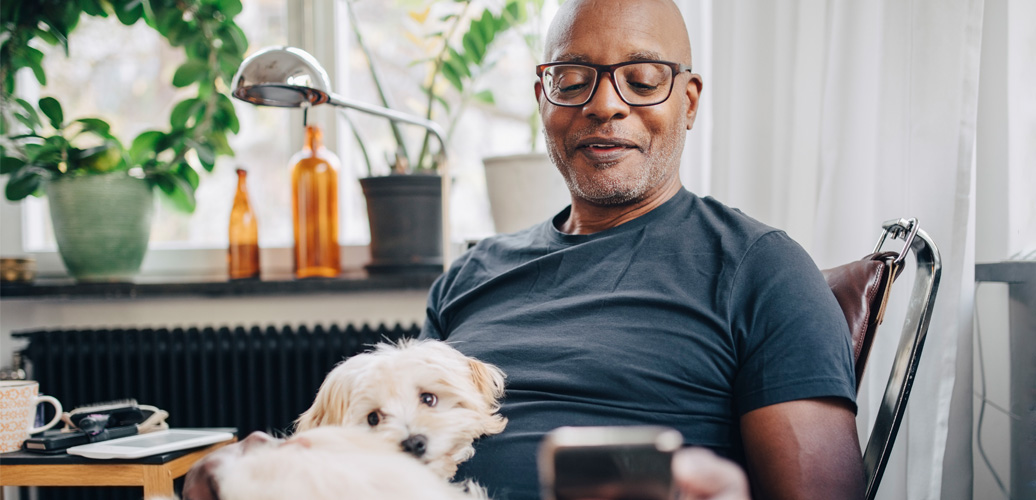 Man with white dog on his lap looking at mobile phone