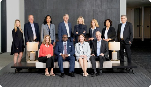Thrivent's executive board sitting and standing around a couch while smiling