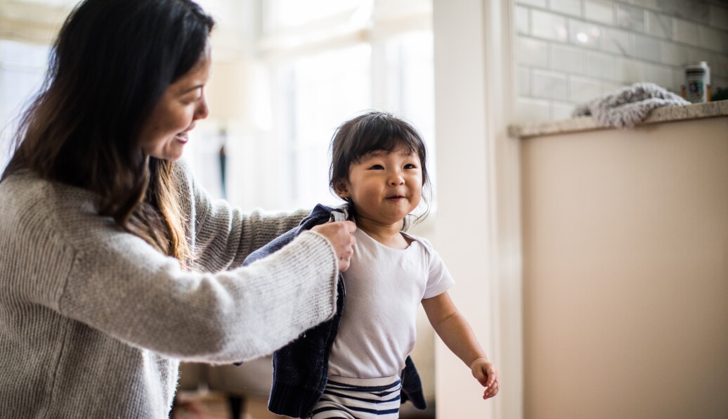 Mother helping daughter (2yrs) put on coat