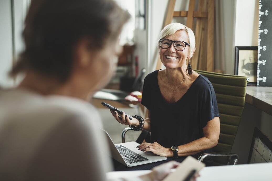 Woman smiling at another person with computer and phone in hand