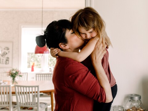adult woman holding toddler up and kissing on their cheek