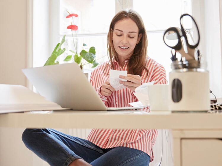 young woman looking at receipts and doing finances on laptop