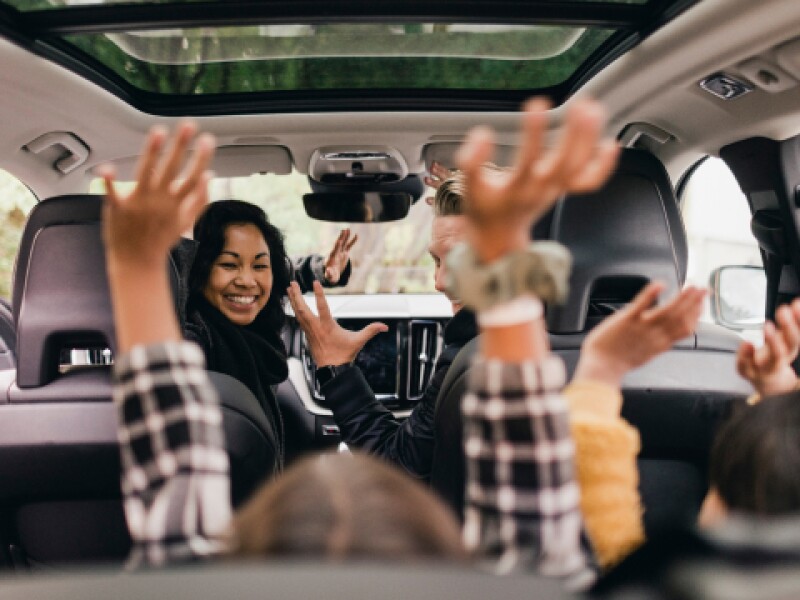 photo of woman in van gleefully looking back at children with their hands up