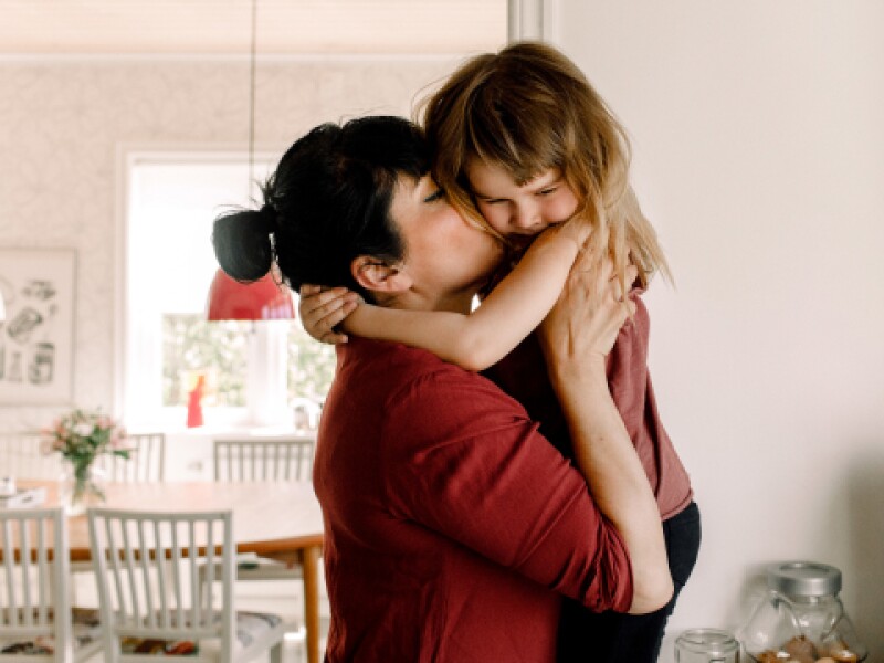 adult woman holding toddler up and kissing on their cheek