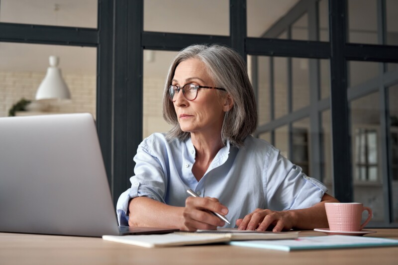 Serious mature older adult woman on laptop working from home or in office.