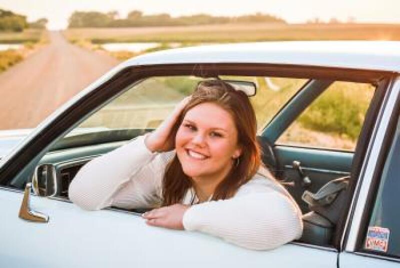 A headshot of Alivia Baumgarn in a blue car parked on a country road