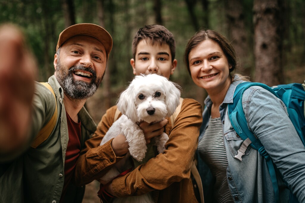 Happy man taking selfie while hiking with family and dog in forest