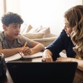 Mother homeschooling teenage boy in front of laptop