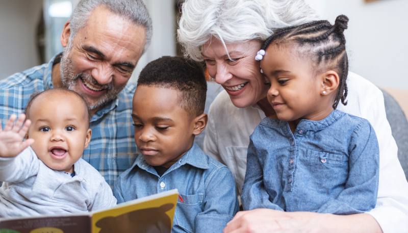 Grandmother and grandfather reading a book with three young grandchildren