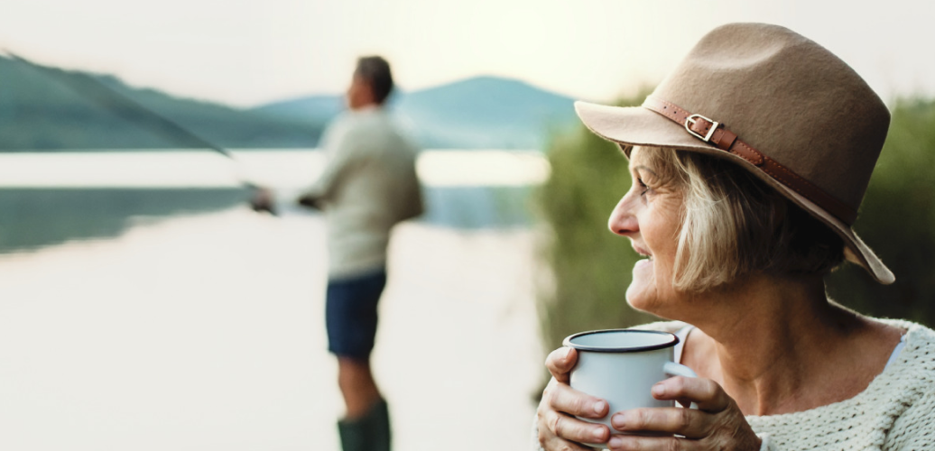 Woman holding coffee cup looks on as her husband fishes