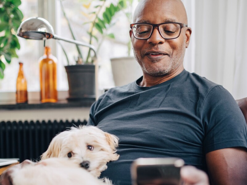 Man with white dog on his lap looking at mobile phone