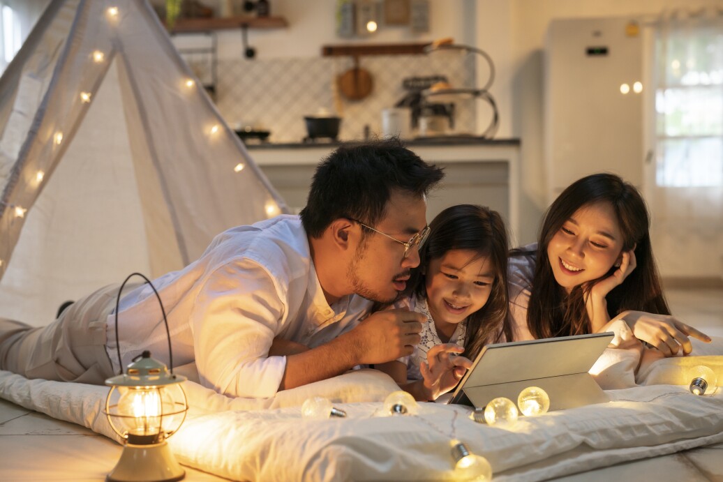 Smiling father looking at daughters using digital tablet in illuminated tent
