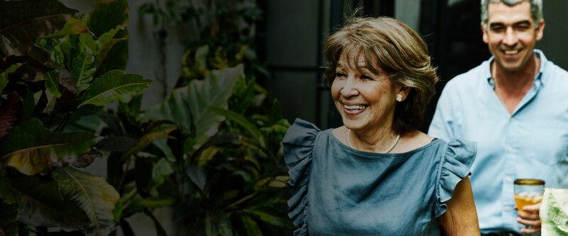 An older man and woman walk out into a leafy garden space, smiling