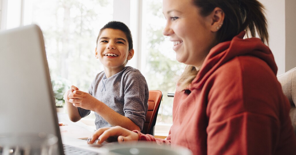 Mother using laptop while sitting with happy autistic son in living room at home