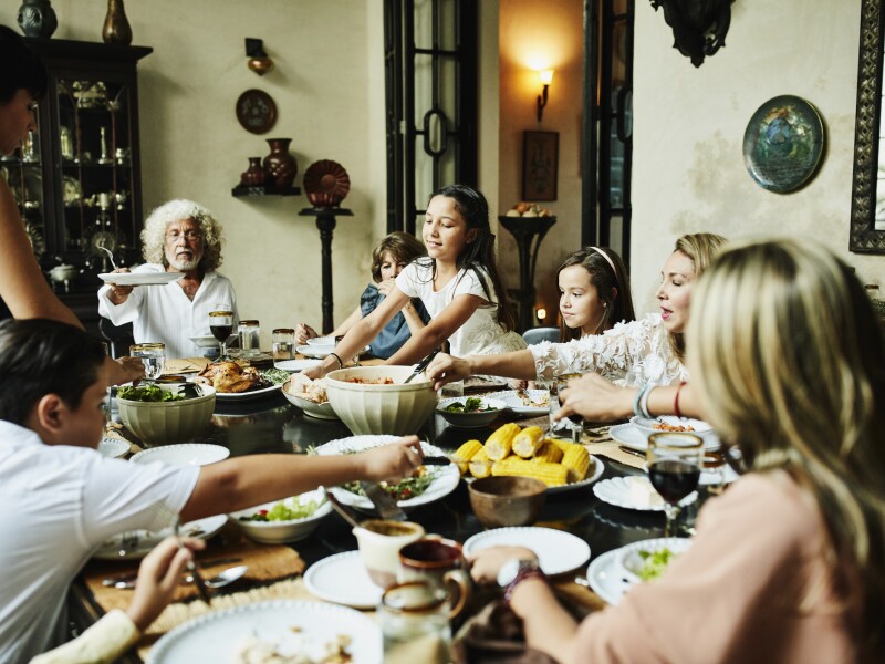 Young girl bringing platter of bread to dining room table during family celebration meal