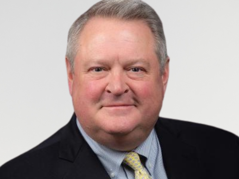 Head shot photo for Dr. Kirk Farney, wearing a navy suit, blue and white striped shirt and yellow tie