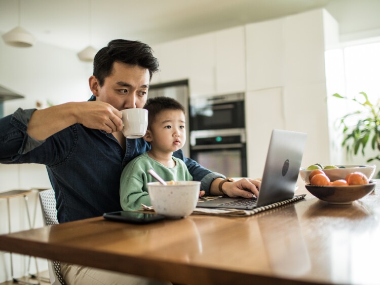 Father multi-tasking with young son (2 yrs) at kitchen table