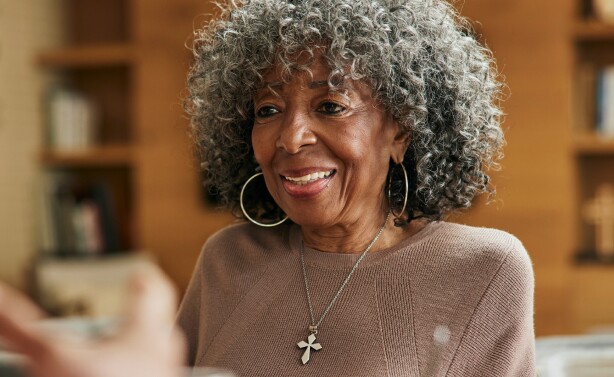 Mature woman with curly gray hair and a cross necklace