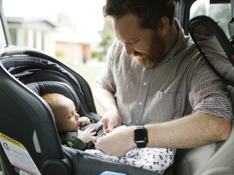 Father buckling baby boy (2-3 months) in car seat