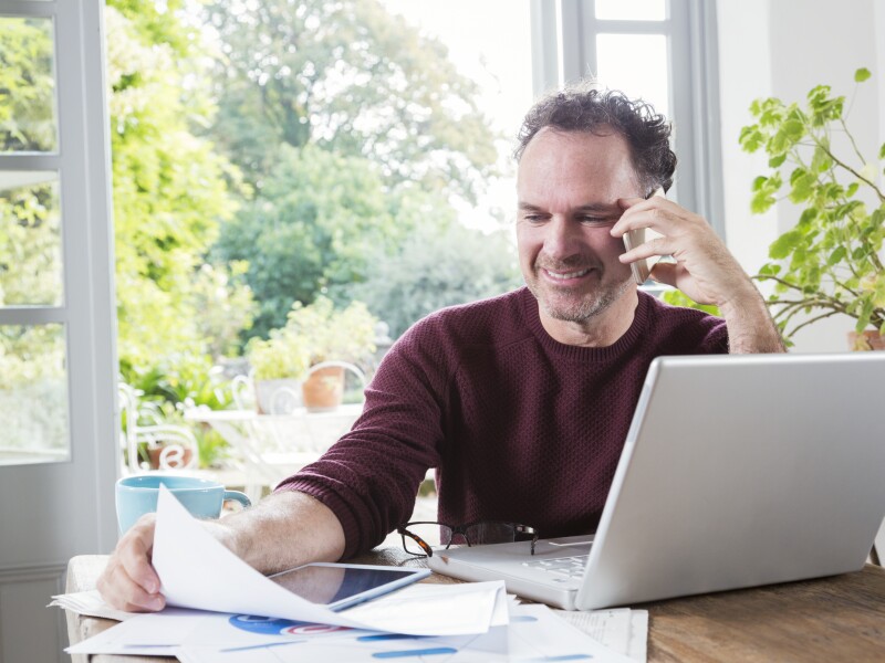Businessman using laptop paying bills online in kitchen