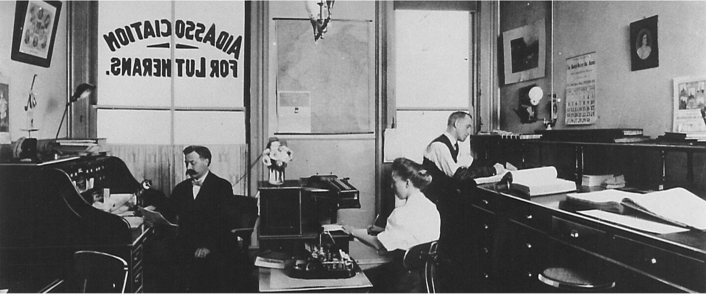 Historical black and white photo of two men and a woman working in the Aid Association for Lutherans office