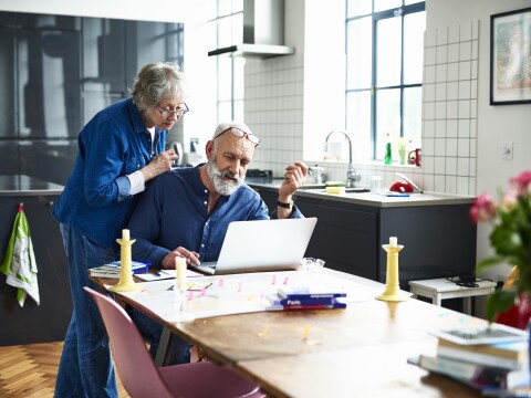 Senior couple planning vacation with map and laptop on table