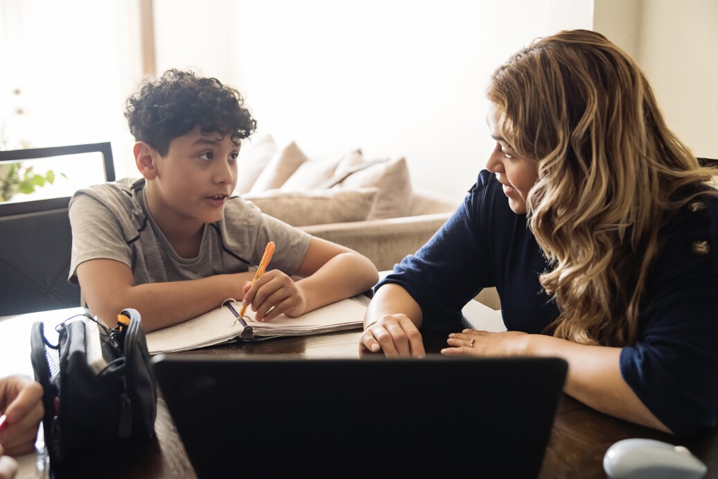 Mother homeschooling teenage boy in front of laptop