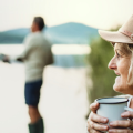 Woman holding coffee cup looks on as her husband fishes