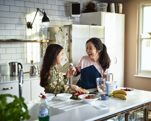 Mother teasing daughter in kitchen whilst making smoothies