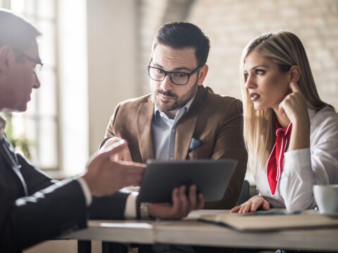 Young couple and their financial advisor looking at touchpad in the office.
