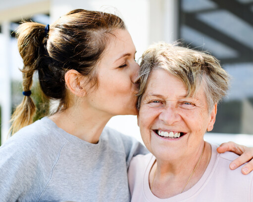 Adult daughter kissing senior mother on the side of the head