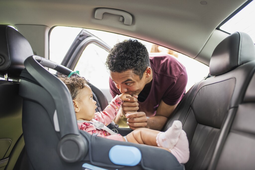 Young father putting baby girl in car seat