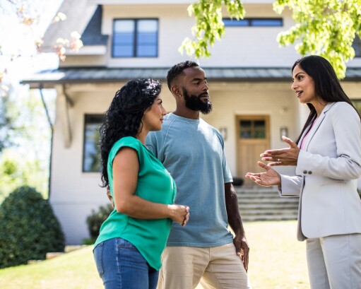 Couple meeting with real estate agent in front of home