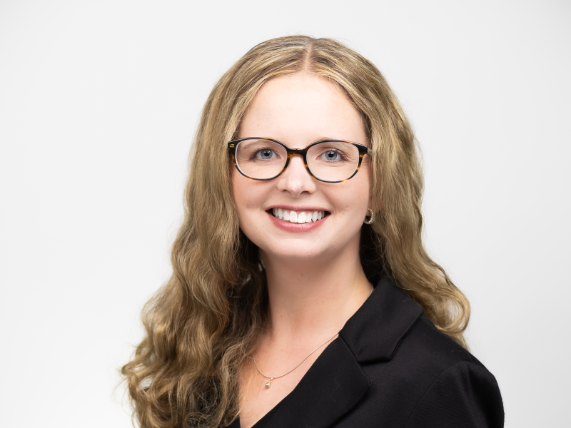 head shot of Emily Yohe, woman in black suit smiling and wearing glasses