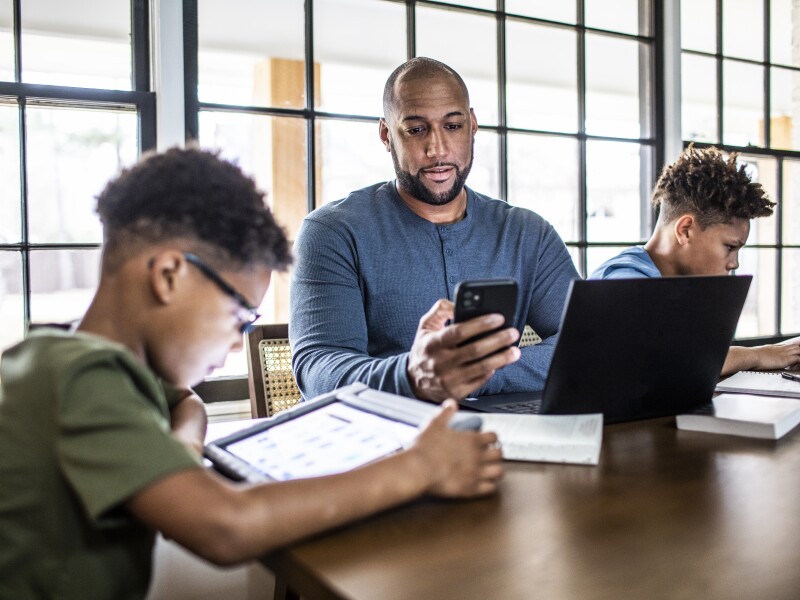 Father working from home in residential kitchen with family in background
