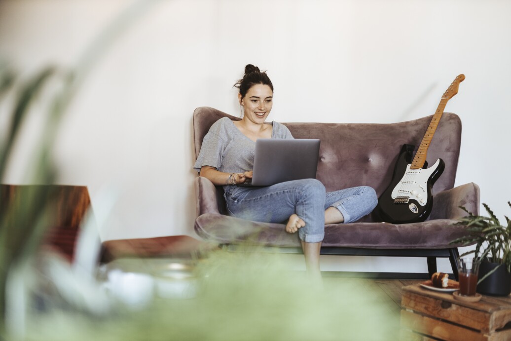 Portrait of smiling young woman sitting on couch at home using laptop