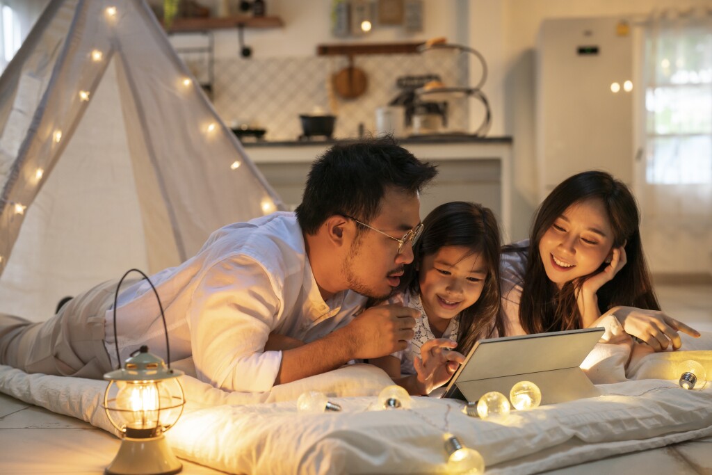Smiling father looking at daughters using digital tablet in illuminated tent