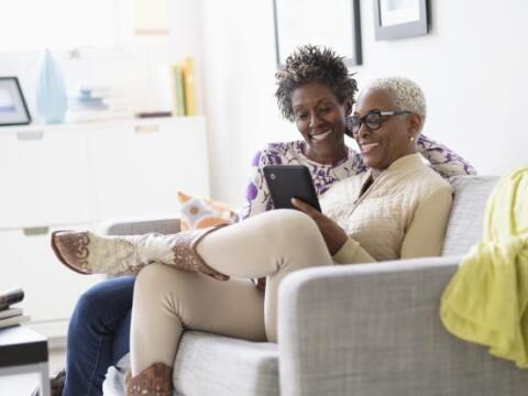 An older woman and her adult daughter smiling at a tablet on the couch