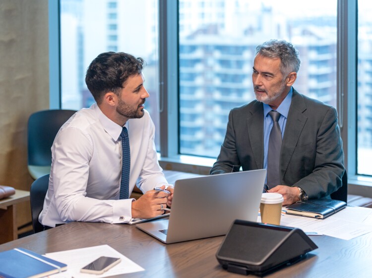Two business men talking and working on a laptop computer in the office.