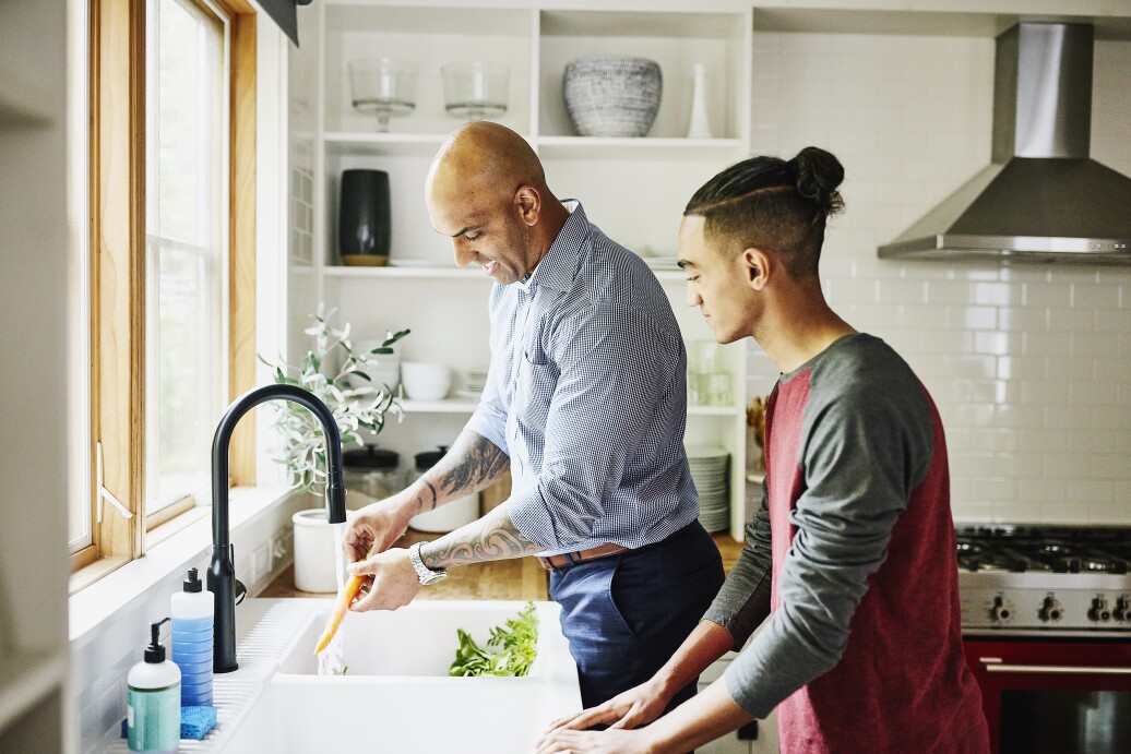 Shot of smiling father and teenage son washing fresh vegetables in kitchen sink