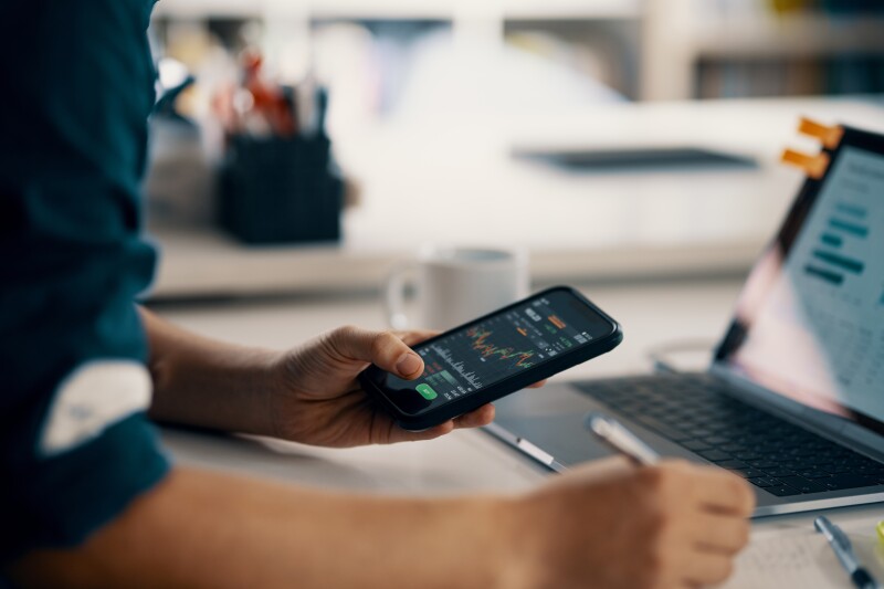 Person viewing phone and laptop with investment information.