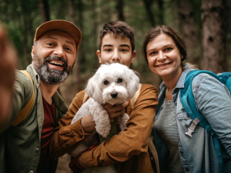 Happy man taking selfie while hiking with family and dog in forest