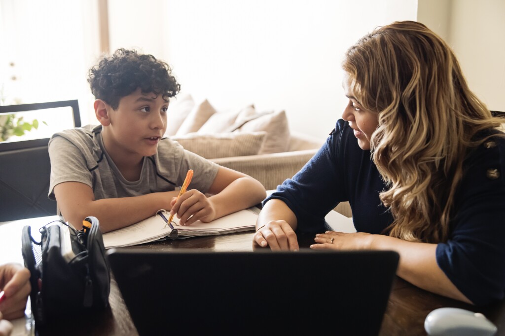 Mother homeschooling teenage boy in front of laptop