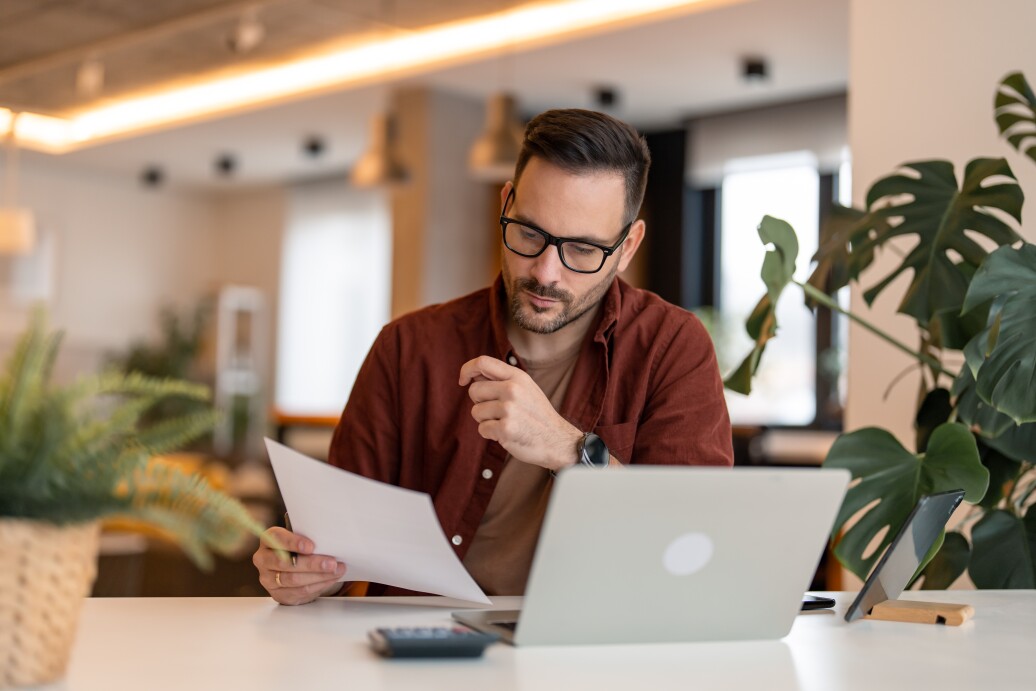 Millennial man using laptop sitting at the table in a home office