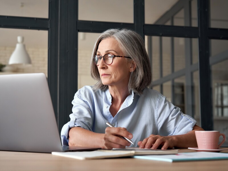 Serious mature older adult woman on laptop working from home or in office.