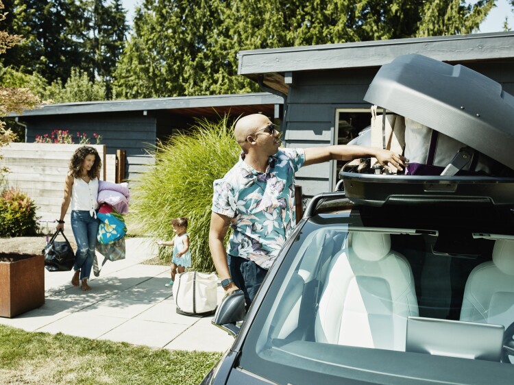Family loading luggage into car top box before road trip